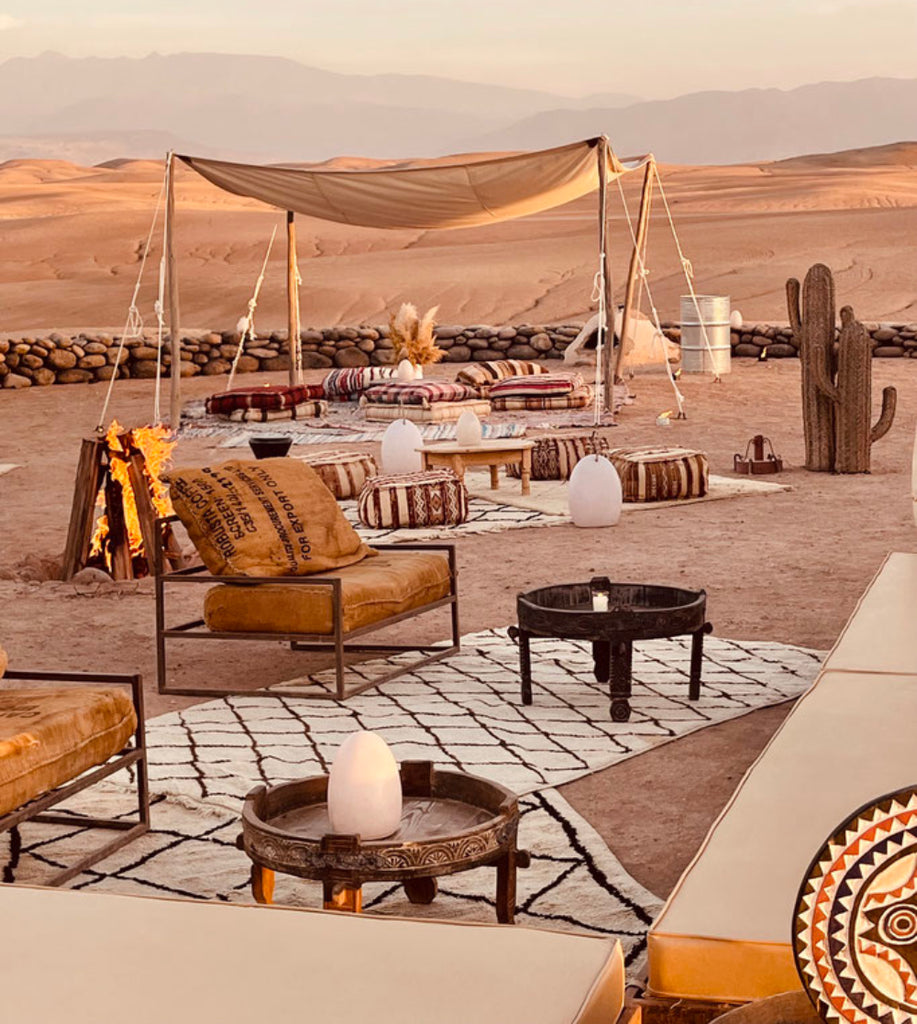 Jardin extérieur dans le désert du marroc, avec des cousins et des canapés confortable pour appécier la brise et le calme de ce décor de rêve. Un parfum boisé et oriental enveloppe l'atmosphère. C'est la fragrance Larme du Sahara de Erra. Disponible en diffuseur et bougie.