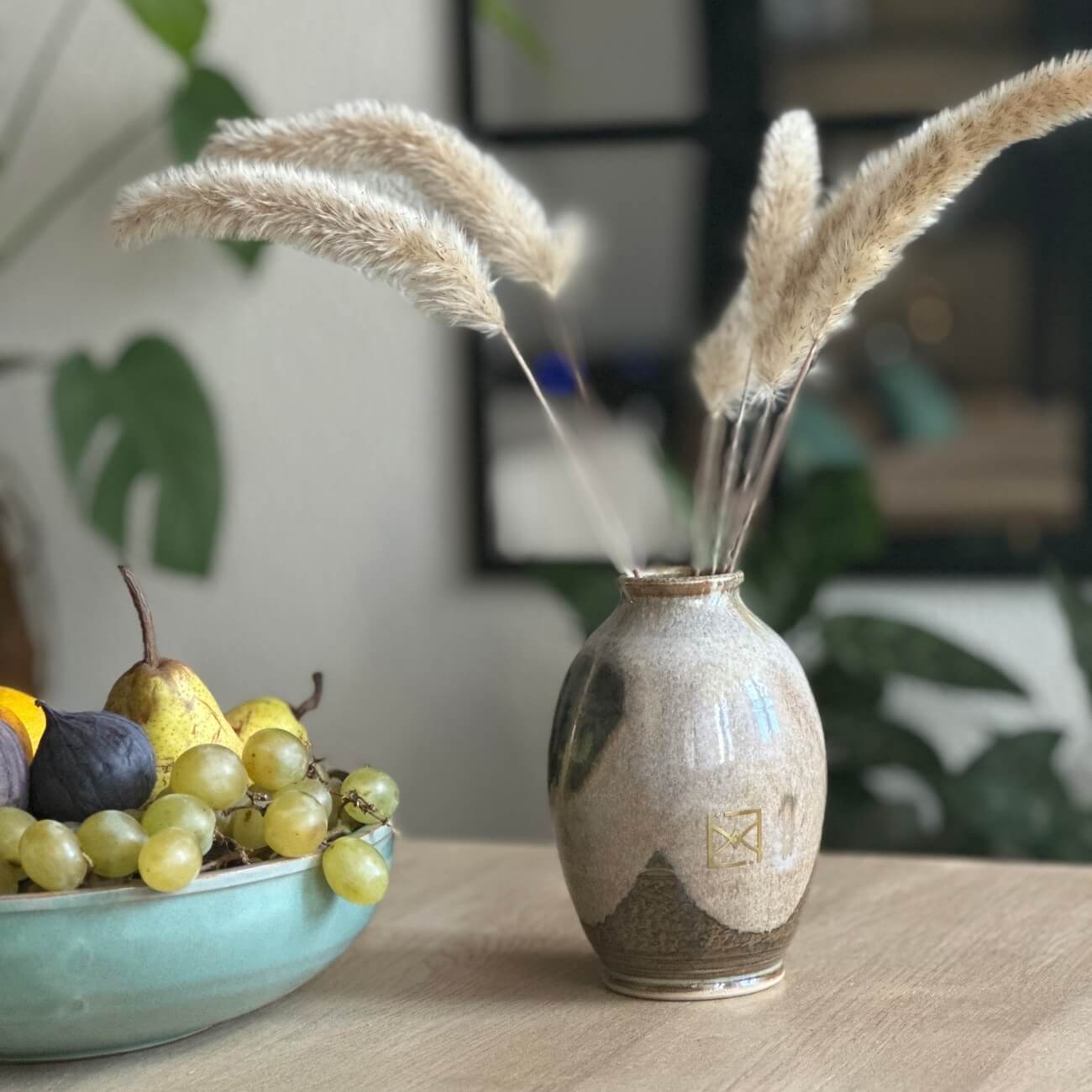 Diffuseur de parfum en céramique brun et beige avec plumes décoratives, déposé à côté d'un bol de fruits sur table en bois, donne une ambiance sophistiqué et chaleureuse.