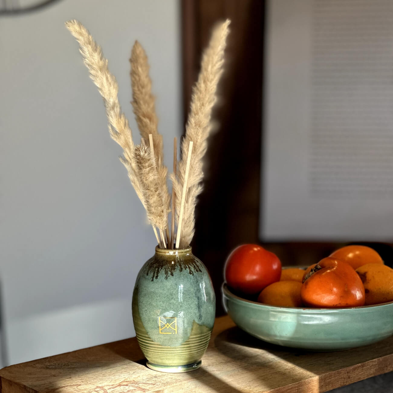 Diffuseur de parfum en céramique verte avec plumes décoratives et bol de fruits sur table en bois
