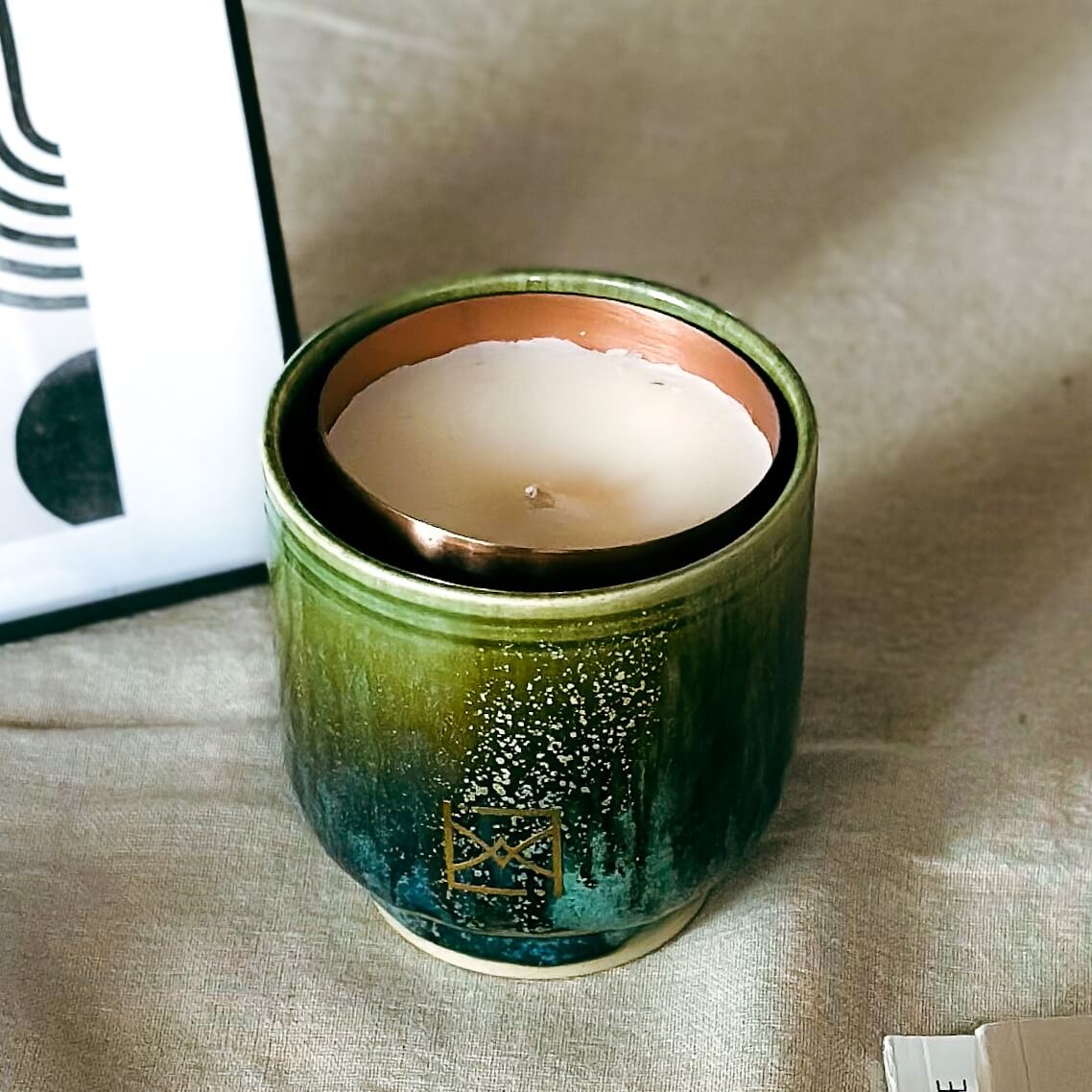 Bougie parfumée en céramique verte et bleue, fabriquée à la main par un artisan suisse pour ERRA, posée sur un tissu beige.