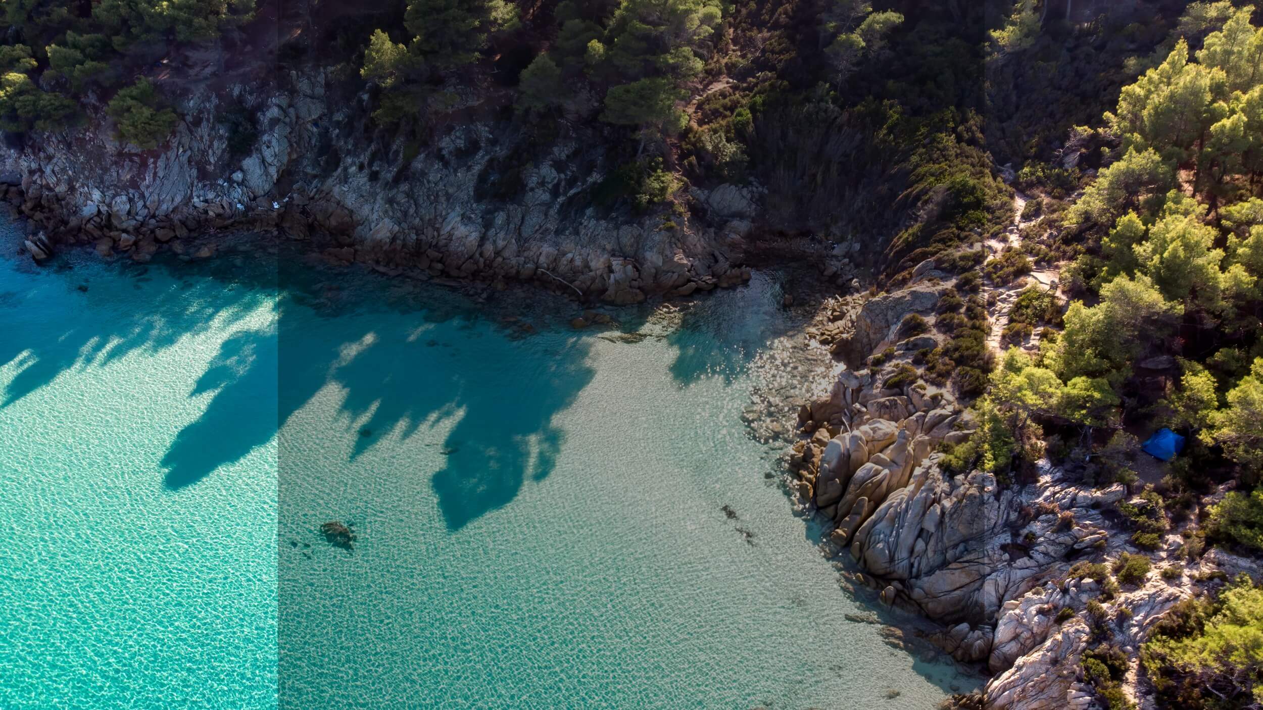 Vue aérienne d’une calanque méditerranéenne bordée de pins et de rochers, eau turquoise cristalline, lumière d’été, végétation sauvage, senteur florale et marine, parfum frais et solaire, paysage côtier préservé, ambiance estivale entre terre et mer.